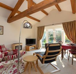 A living room with wooden beams a sofa a TV and a dining table with chairs at Bank Foot in Ambleside