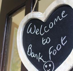 A heart shaped chalkboard sign hanging on a door with welcome to Bank Foot written on it at Bank Foot in Ambleside