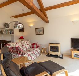 A living room with wooden beams a floral sofa a black leather chair a small fireplace and a television at Bank Foot in Ambleside