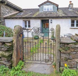 The front view of a stone cottage with a green door behind a black iron gate and stone wall at Janes Cottage in Hawkshead