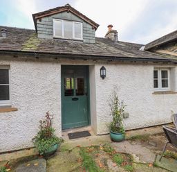 An exterior view of a cottage with a green door two windows two potted plants and outdoor chairs and table at Janes Cottage in Hawkshead