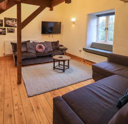 A sitting room with two sofas a round wooden coffee table a wall mounted television and a window seat at Janes Cottage in Hawkshead