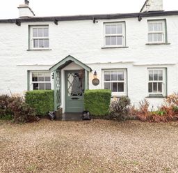 Front facade of a white cottage with green door and windows and bushes at Nurses Cottage Hawkshead