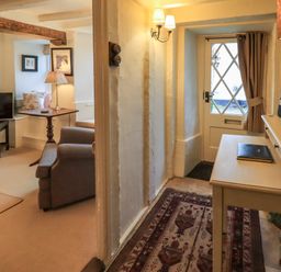 A hallway with a rug and table lamp next to a door and a living room with armchair television and side table at Nurses Cottage in Hawkshead