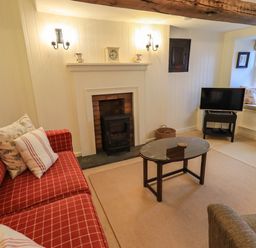 A living room with a red checkered sofa a glass coffee table a fireplace and a television at Nurses Cottage in Hawkshead