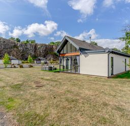 A white house with a slanted roof and large windows on a grassy plot with rock cliffs in the background at Wood Sage in Bamburgh