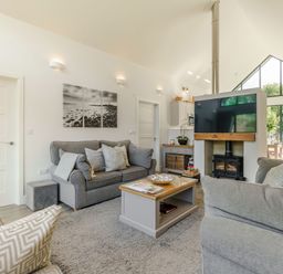 A living room with gray sofas a coffee table a wood stove and large windows at Wood Sage in Bamburgh