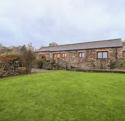 A stone house with multiple windows and a green lawn in front at Low House in Ullswater