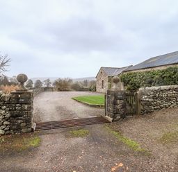 An entrance gate with stone pillars and a cattle grid leading to a stone building and driveway at Low House in Ullswater