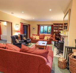 A living room with red sofas two armchairs a wooden coffee table a fireplace and bookshelves at Low House in Ullswater