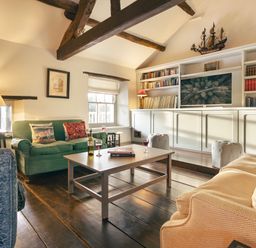 A living room with sofas a coffee table bookshelves and exposed wooden beams at High Lindeth in Bowness