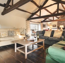 A living room with sofas coffee table wine glasses exposed wooden beams and a stone fireplace at High Lindeth in Bowness