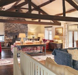 A living room with exposed wooden beams stone fireplace multiple sofas and table lamps at High Lindeth in Bowness