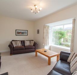 A living room with two leather sofas facing a wooden coffee table and a large window with curtains at The Haven in Keswick