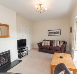 A living room with a brown leather sofa striped cushions a wooden coffee table a television on a stand a fireplace with a mirror above and cream curtains at The Haven in Keswick
