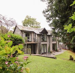 A two-story house with a balcony and patio surrounded by trees and grass at Fir Howe in Skelwith