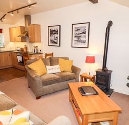 A living room with a sofa wooden coffee table and a wood stove next to an open kitchen at Fir Howe in Skelwith
