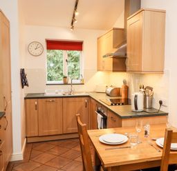 A kitchen with wooden cabinets a dining table set with plates and glasses and a window with a red blind at Fir Howe in Skelwith