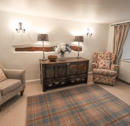 A living room with two armchairs a wooden sideboard with lamps and flowers and a window with curtains at Syke Cottage in Hawkshead