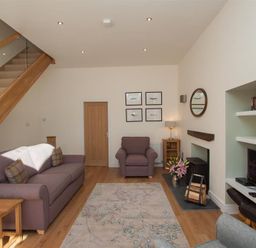 A living room with a sofa armchair rug fireplace recessed shelves and wooden stairs at Mylnbeck in Bowness