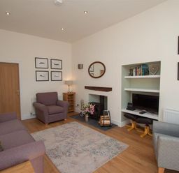 A living room with two armchairs a sofa a rug a fireplace and a built-in shelving unit at Mylnbeck in Bowness
