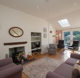 A living room with sofas armchairs a fireplace and glass doors to a garden at Mylnbeck in Bowness