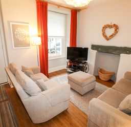 A living room with two sofas a TV on a stand a floor lamp and a window with red curtains at Hazeldene in Ambleside