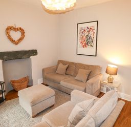 A living room with beige sofas a TV on a stand and a lamp on a side table at Hazeldene in Ambleside