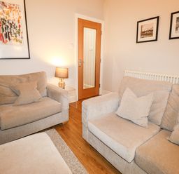 A living room with beige sofas cushions a lamp on a side table wooden flooring and framed pictures on walls at Hazeldene in Ambleside