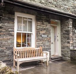 A stone exterior wall with two windows wooden benches and an open door at Hazeldene in Ambleside