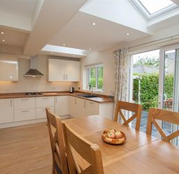 A kitchen with white cabinets wooden countertops a wooden dining table with chairs and a bowl of apples at Fell End in Keswick