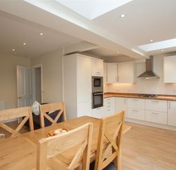 A kitchen with wooden dining table and chairs white cabinets and built in oven at Fell End in Keswick