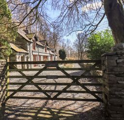 A stone cottage behind a wooden gate with a gravel driveway and trees at The Stables in Ambleside
