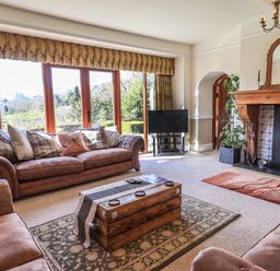 A living room with two sofas a wooden coffee table a fireplace and a television by large windows at The Stables in Ambleside
