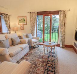 A living room with beige sofas a patterned rug a glass coffee table fireplace and large windows with curtains at Hannakin Barn in Hawkshead