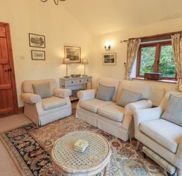 A living room with two armchairs a sofa a round coffee table a wooden door and a window with curtains at Hannakin Barn Hawkshead