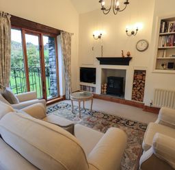 A living room with beige sofas a fireplace built in bookshelves and glass doors at Hannakin Barn in Hawkshead