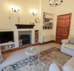 A living room with a fireplace wood stove bookshelf sofa armchair and wooden door at Hannakin Barn in Hawkshead
