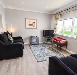A living room with black sofas a small table a television and a window with curtains at Fairview in Bowness