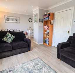 A living room with two black sofas a green patterned cushion a wooden bookshelf and a wall clock at Fairview in Bowness