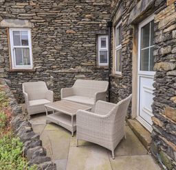 A stone exterior seating area with wicker chairs and a table outside a building at Gildabrook Cottage in Bowness