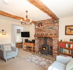 A living room with a brick fireplace wood burning stove two armchairs a bookshelf and a television at Hodge How Cottage in Windermere