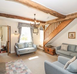 A living room with blue sofas a wooden chest under stairs and exposed wooden beams at Hodge How Cottage in Windermere