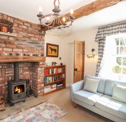 A living room with a brick fireplace wood stove bookshelf and blue sofa at Hodge How Cottage in Windermere