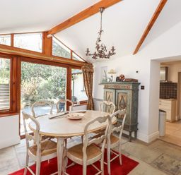 A dining room with wooden table and chairs and large windows overlooking garden at Hodge How Cottage in Windermere