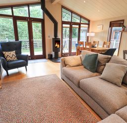 A living room with a sofa pillows armchair wood burning stove dining table and windows at Beck of Beyond in Ambleside