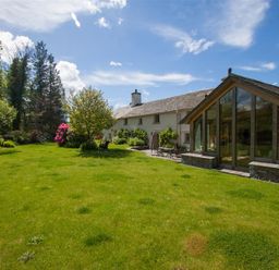 A garden with green grass trees and flowering shrubs outside a house with large glass windows at Old Droomer in Windermere