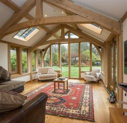 A sitting room with wooden beams large windows armchairs and a patterned red rug at Old Droomer in Windermere