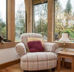 A plaid armchair with cushions next to a wooden side table with a lamp in a room with large windows at Old Droomer in Windermere