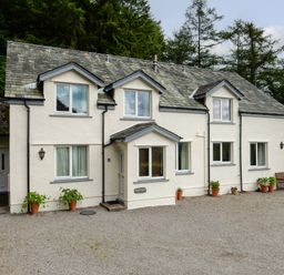 A white two-story house with multiple windows and potted plants on a gravel driveway at Kirkstones in Keswick